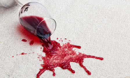 Bild von einem umgekipptem Weinglas und verschüttetem Rotwein auf einem weißen Teppich.